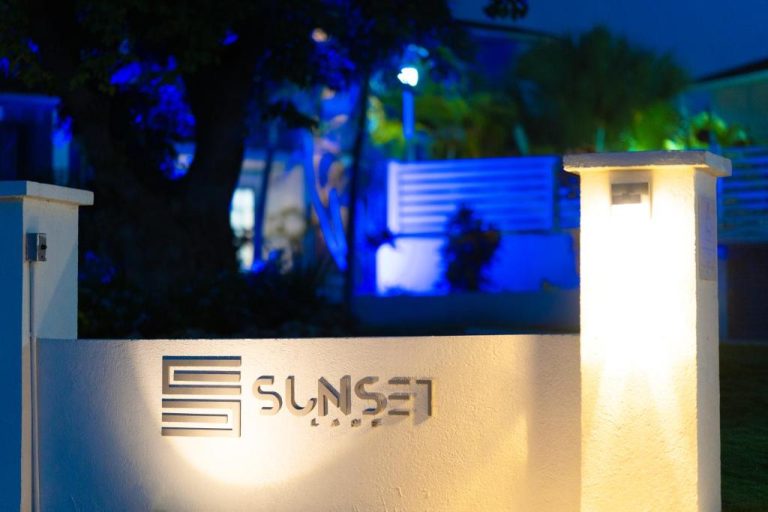 Entrada principal iluminada del Sunset Lane Apartment Hotel durante la noche con cartel corporativo