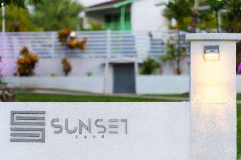 Entrada principal con cartel iluminado del Sunset Lane Apartment Hotel y jardines exteriores