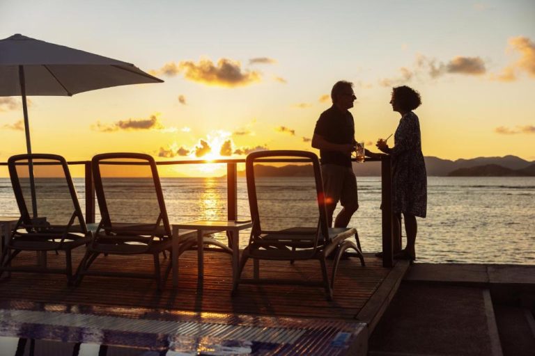 Pareja disfrutando de la puesta de sol con cócteles en la terraza frente al mar del Le Nautique Waterfront Hotel La Digue