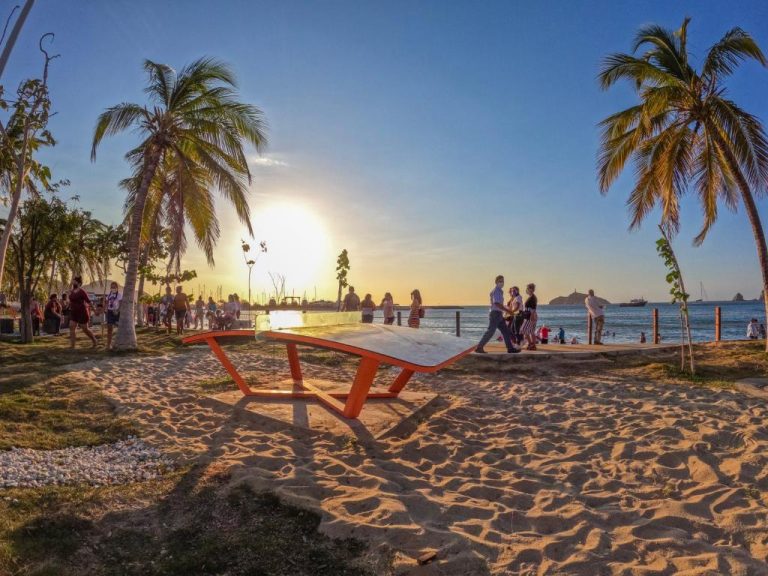 Atardecer en la playa del Azure Apartahotel con palmeras, mesa de ping pong y turistas disfrutando del mar