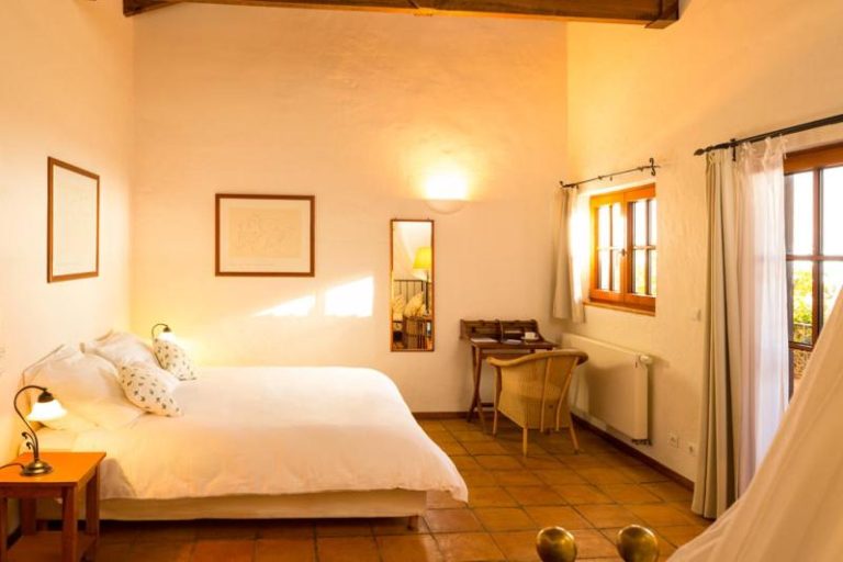 Habitación doble con decoración rústica y cama blanca en el Hotel Atrio, con suelo de barro y ventana con luz natural