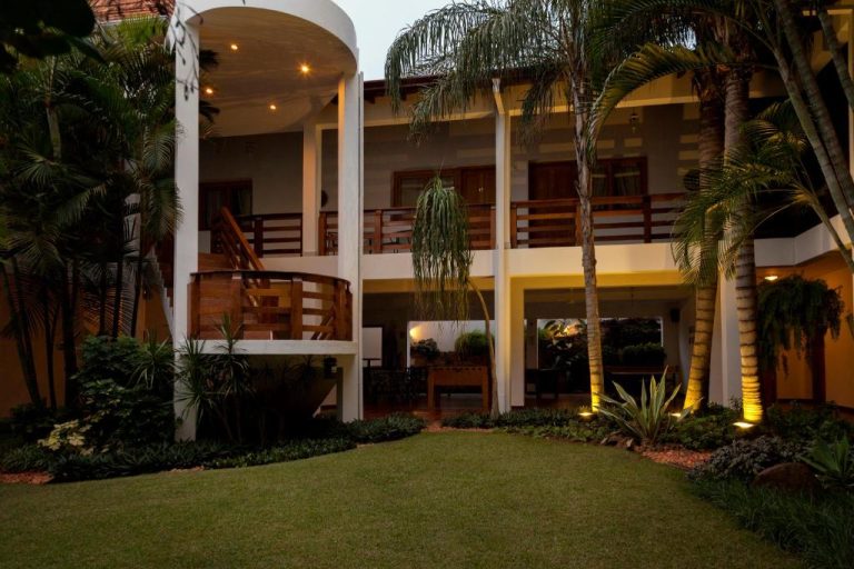Jardín exterior con palmeras y balcones de madera del Hotel Westfalenhaus al atardecer