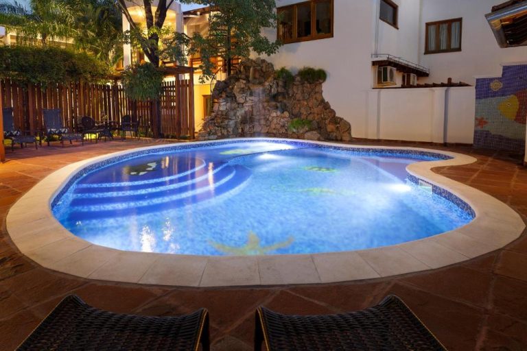 Piscina exterior iluminada con cascada de piedra natural del Hotel Westfalenhaus al anochecer