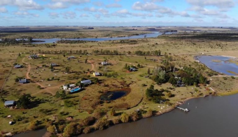 Vista aérea del Complejo La Posta del Hum con cabañas, laguna y acceso al río rodeado de naturaleza