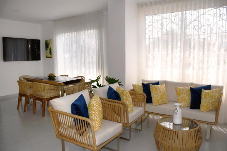 Sala de estar y comedor del Azure Apartahotel con sofás de ratán y cojines azules y amarillos
