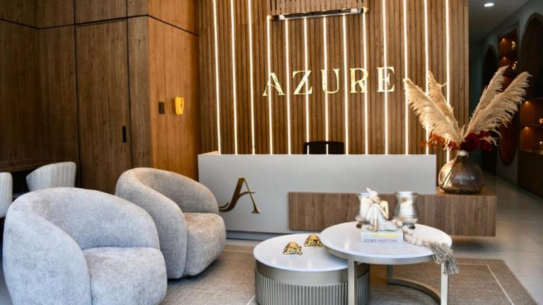 Recepción moderna del Azure Apartahotel con sillones grises, mesa decorativa y pared de madera iluminada