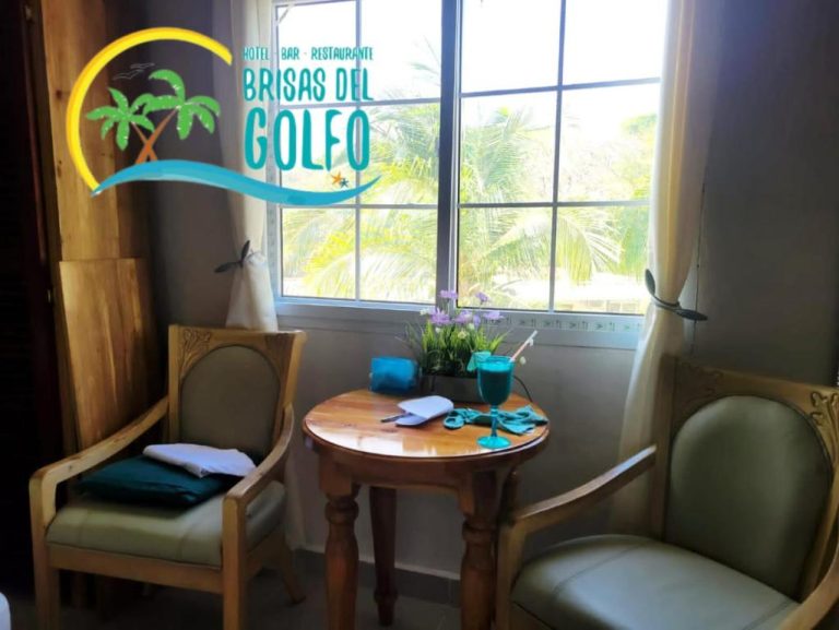 Habitación con sillas y mesa de madera junto a ventana con vista a palmeras en Hotel Brisas del Golfo