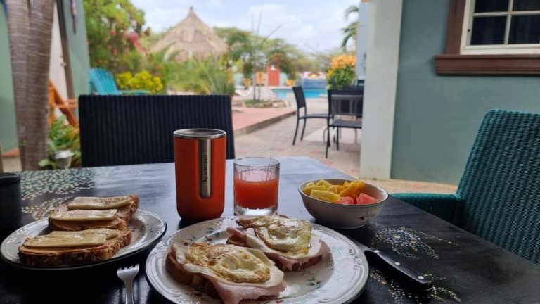 Desayuno con huevos, tostadas y zumo de frutas en la terraza con piscina de La Felicidad Aruba
