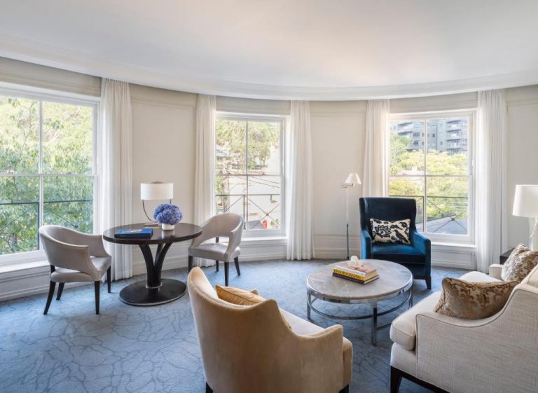 Elegante salón de suite con ventanales y decoración en azul del The Langham Sydney