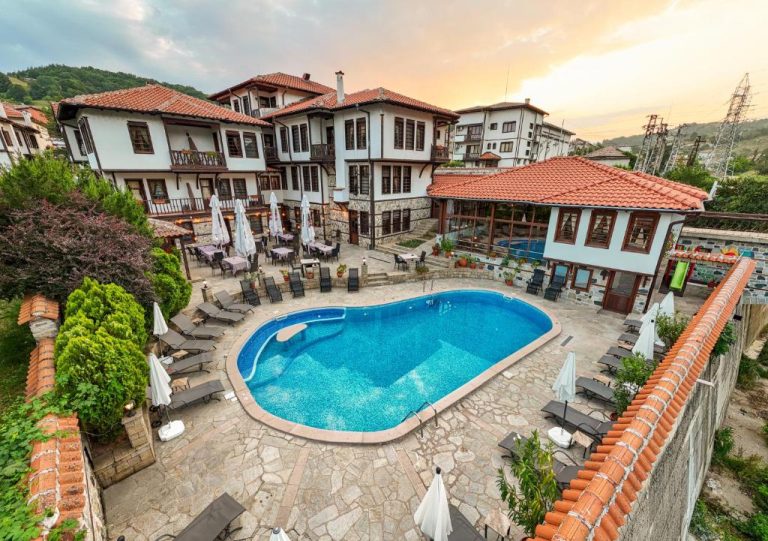 Piscina exterior con tumbonas y sombrillas del Spa Complex Aleksandar rodeado de casas tradicionales