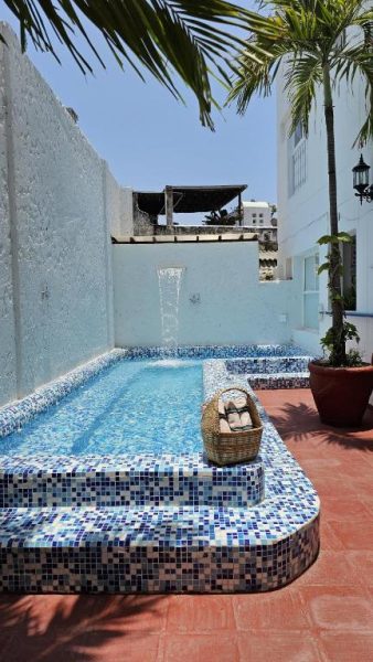 Piscina con mosaicos azules y cascada decorativa en el Hotel Kartaxa, rodeada de terracota y palmeras