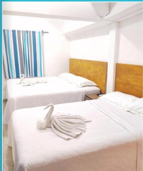 Habitación triple con camas blancas y decoración de cisnes hechos con toallas en Íkaro Suites Cancún