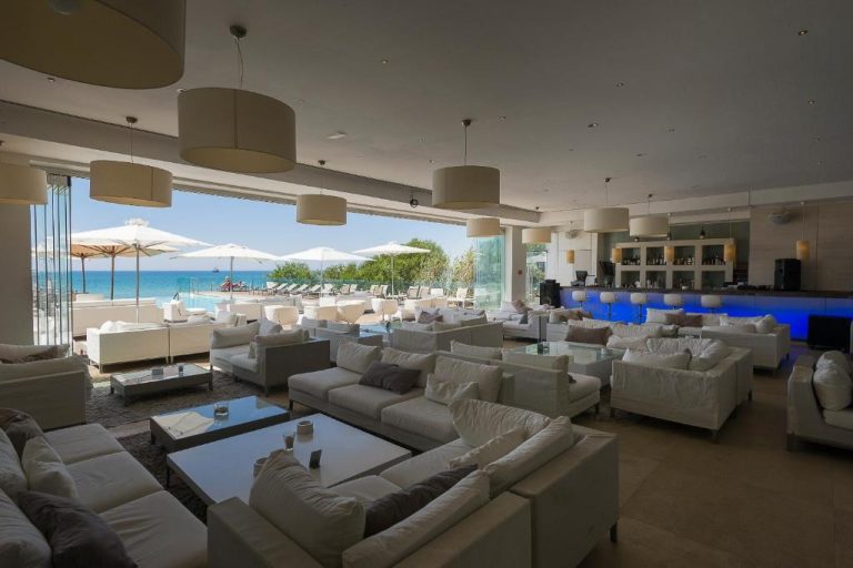 Elegante lobby bar con sofás blancos y vistas al mar y piscina exterior en The Sindbad Hotel