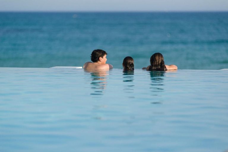 Tres personas disfrutando de la piscina infinita con vistas al mar en The Sindbad
