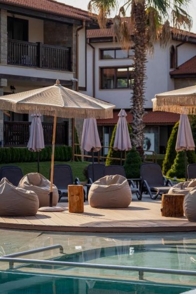 Zona de piscina con puffs y sombrillas de paja en Boutique Complex Trakiets Bulgaria