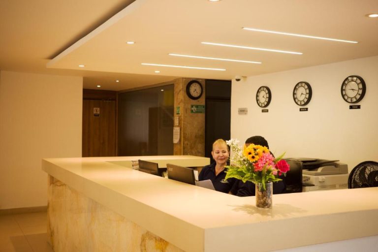 Recepción moderna del Hotel La Riviera con relojes internacionales y arreglo floral colorido en el mostrador