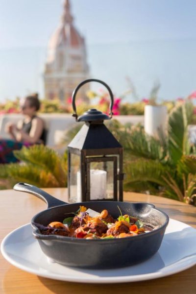 Plato gourmet en sartén de hierro en la terraza del Movich Hotel Cartagena de Indias con vista a la catedral
