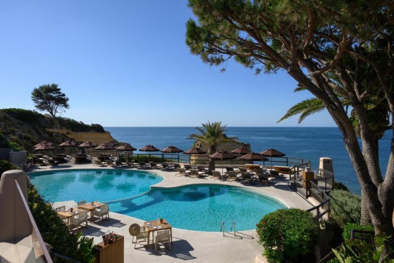 Piscina exterior con vistas al mar y tumbonas con sombrillas en Vilalara Grand Hotel Algarve