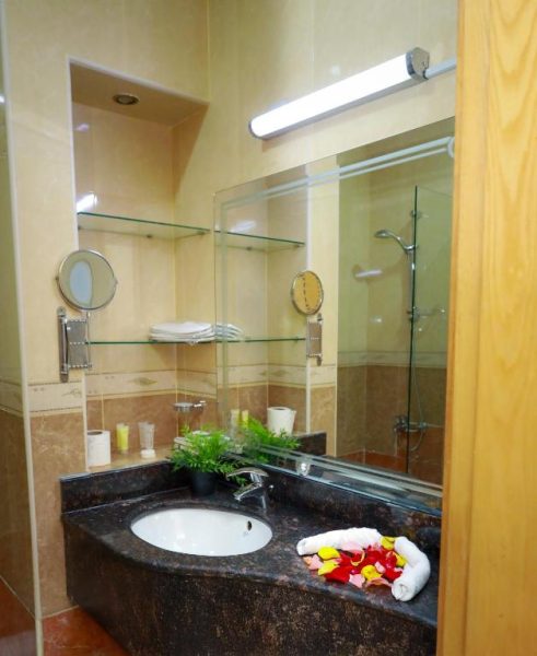 Baño elegante con ducha de cristal y encimera de mármol oscuro en el Doha Dynasty Hotel
