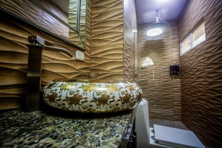 Lavabo artesanal dorado con motivos florales sobre encimera de mármol en el baño de lujo del Hotel Bugambilias