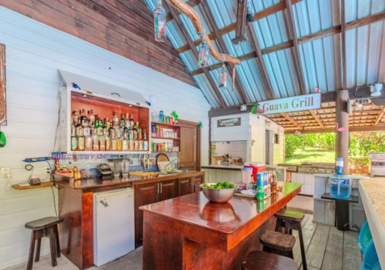 Bar tropical Guava Grill con barra de madera y estantes de bebidas en Guava Grove Resort & Villas