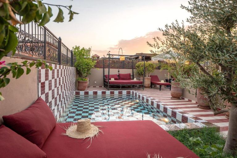 Terraza con piscina de mosaicos y zona de descanso con cojines rojos en Riad Tassili Boutique