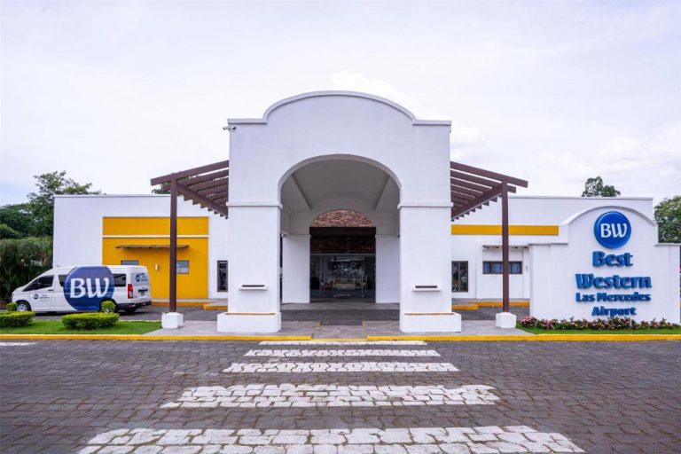 Fachada principal y entrada del Best Western Las Mercedes Airport con arco blanco y furgoneta de traslado