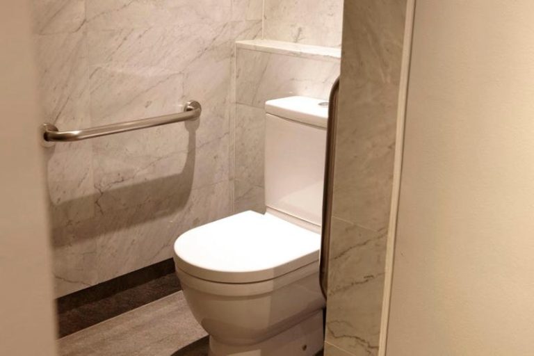 Baño accesible con paredes de mármol blanco y barra de apoyo en The Singular Santiago