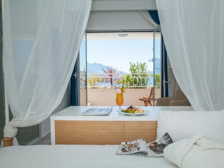 Habitación con dosel blanco y balcón con vistas al mar y montañas en Boutique Hotel Blanc & Bleu
