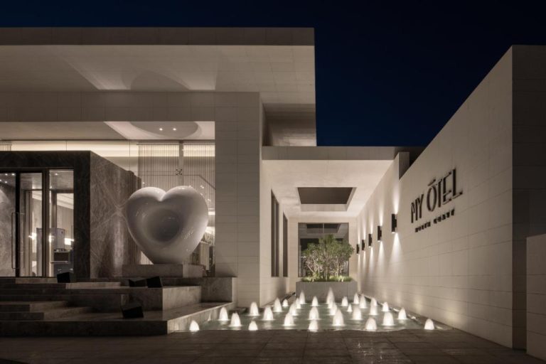 Entrada iluminada de noche con fuentes y escultura de corazón en My Ōtel North Coast Adult Only