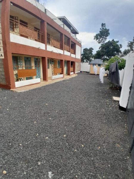 Patio exterior con gravilla y fachada de dos plantas del hotel Villa De Leo en África