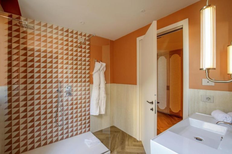 Baño moderno con ducha y azulejos geométricos naranjas del Rosetta Hotel Perugia Tapestry Collection by Hilton