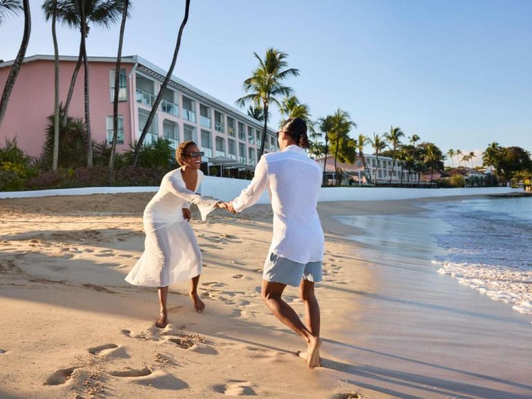 Pareja paseando de la mano en la playa del Fairmont Royal Pavilion Barbados Resort al atardecer