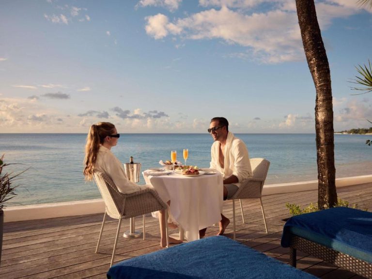 Pareja desayunando con champán en terraza frente al mar en Fairmont Royal Pavilion Barbados Resort
