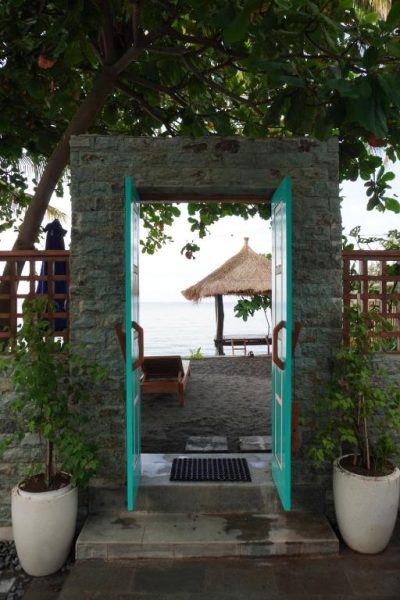 Puerta turquesa con acceso directo a la playa del Tasola Boutique Hotel con palapa y tumbonas