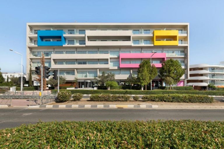 Fachada exterior del UC Hall Residence con balcones en azul, amarillo y rosa en edificio moderno