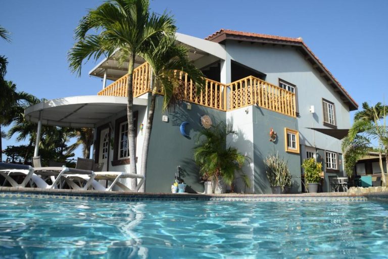 Piscina exterior con terraza y palmeras de La Felicidad Aruba, villa con balcón de madera