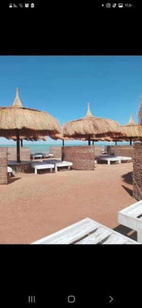 Sombrillas de paja y tumbonas en la playa de la aldea Fanadir Bay en Hurghada, Egipto