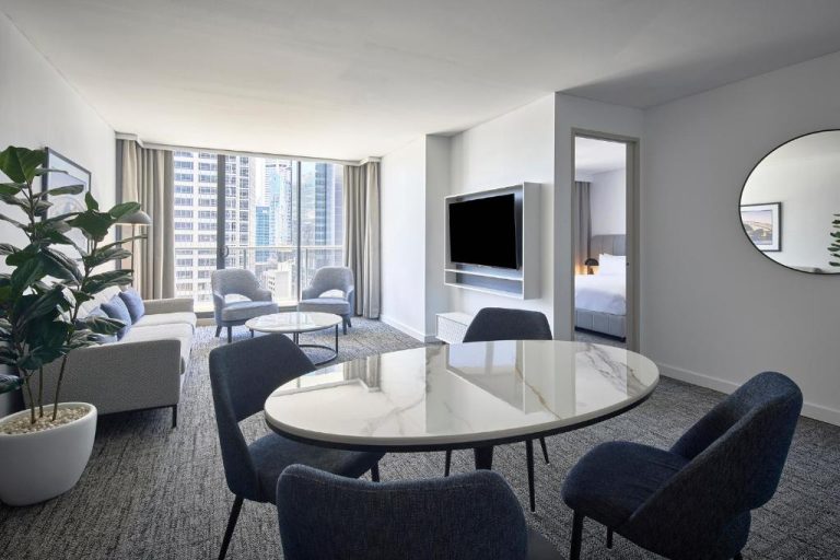 Suite con sala de estar moderna y vistas al skyline de Sídney en Meriton Suites Pitt Street