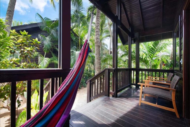 Terraza con hamaca colorida y sillas de mimbre rodeada de vegetación tropical en Hotel Puerta Azul
