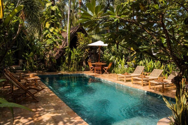 Piscina exterior rodeada de jardín tropical con tumbonas de madera en el hotel Selvática