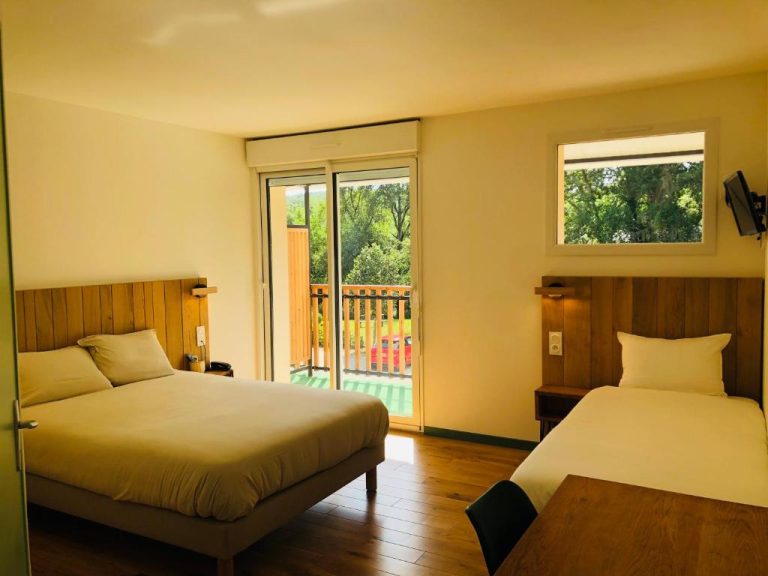 Habitación twin con dos camas y balcón con vistas al jardín en Logis Hôtel Les Tilleuls