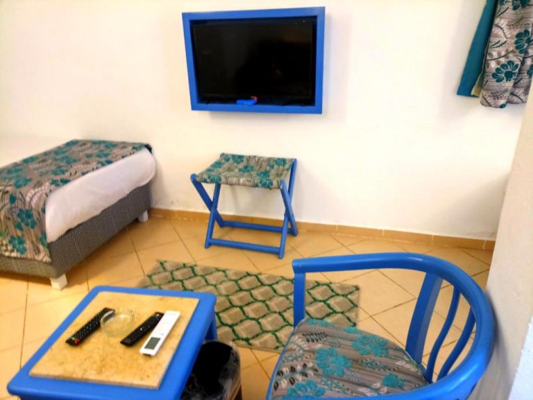Habitación del Kanabesh Hotel con TV de pared, sillas azules, mesa auxiliar y cama individual
