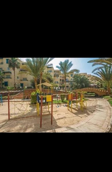 Área de juegos infantil con columpios y toboganes en la aldahabia village rodeada de palmeras
