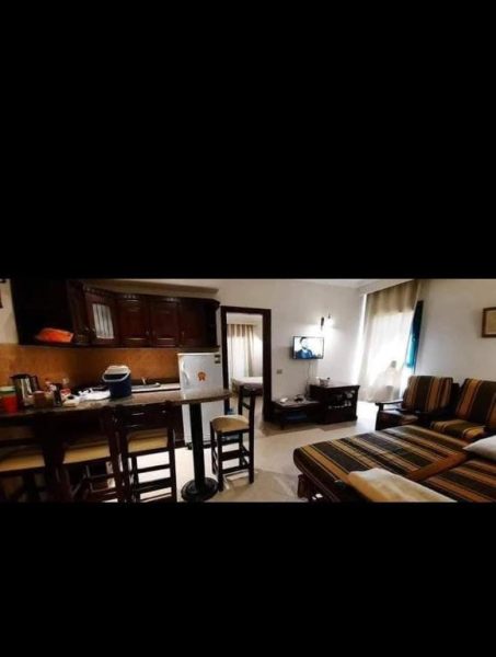 Salón con cocina americana y zona de estar en la Qariat Al Dahabia, con muebles de madera y televisión