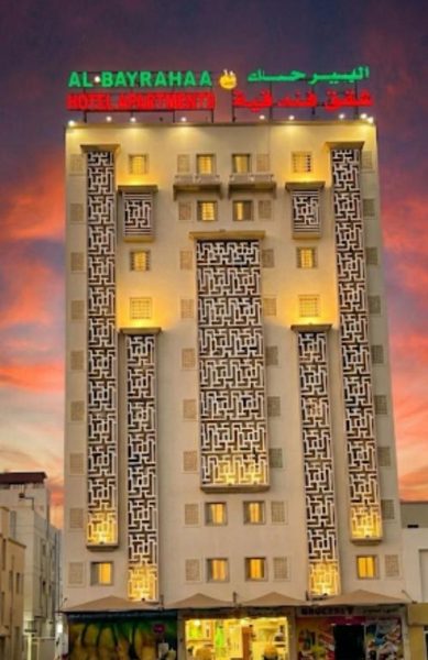 Fachada exterior iluminada del Al-Bayraha Hotel Apartments con decoración árabe tradicional al atardecer