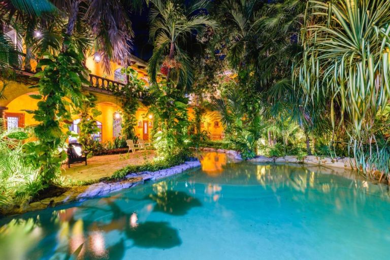 Piscina tropical iluminada de noche rodeada de vegetación exuberante en La Hacienda Hotel at Xcaret
