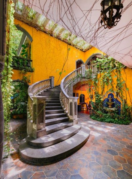 Espectacular escalera curva colonial con paredes amarillas y vegetación tropical en La Hacienda Hotel at Xcaret