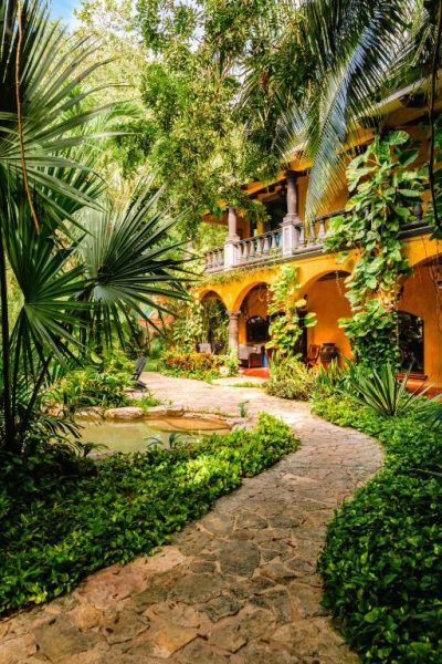 Jardín tropical con camino de piedra y patio colonial en La Hacienda Hotel at Xcaret, México