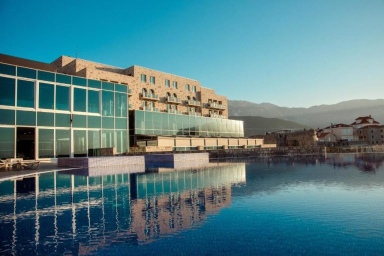Piscina exterior con reflejo de la fachada acristalada del Avala Resort & Villas en Montenegro